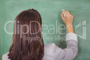 Rear view of teacher writing on chalkboard in a classroom
