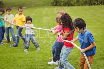 Cute pupils playing tug of war on the grass outside