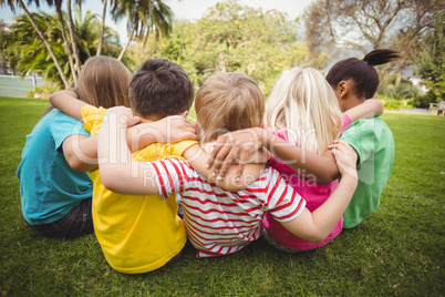 Happy classmates sitting in grass and having arms around