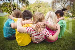 Happy classmates sitting in grass and having arms around