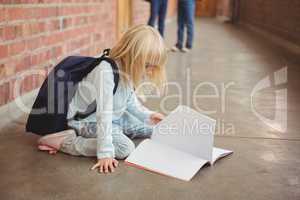Cute pupil kneeling over notepad at corridor