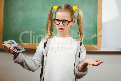 Confused cute pupil holding calculator in a classroom