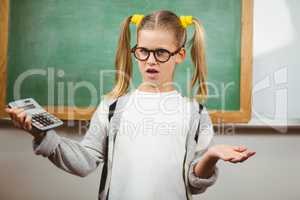 Confused cute pupil holding calculator in a classroom