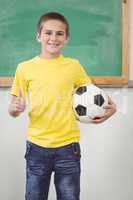 Smiling pupil holding football in a classroom
