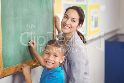 Pretty teacher helping pupil at chalkboard