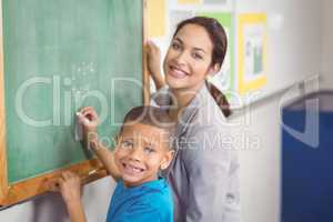 Pretty teacher helping pupil at chalkboard