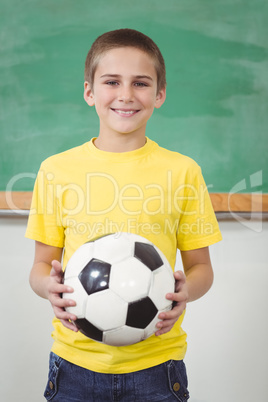 Smiling pupil holding football in a classroom