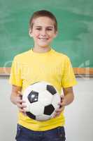 Smiling pupil holding football in a classroom