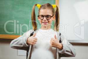 Cute pupil doing thumbs up in front of chalkboard
