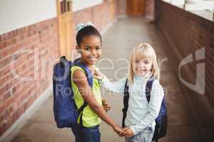 Smiling pupils holding hands at corridor