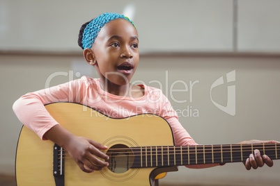 Cute pupil singing and playing guitar in a classroom