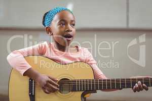 Cute pupil singing and playing guitar in a classroom