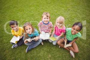 Smiling classmates sitting in grass and holding books