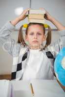 Cute pupil balancing books on head in a classroom