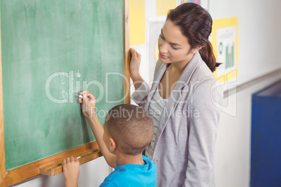 Pretty teacher helping pupil at chalkboard