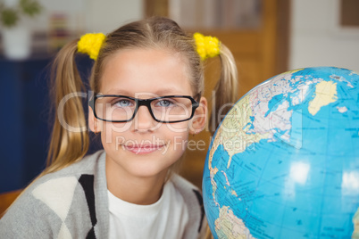 Cute pupil smiling next to globe in a classroom