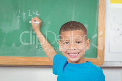 Cute pupil writing on chalkboard in a classroom