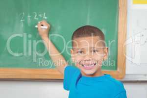 Cute pupil writing on chalkboard in a classroom