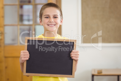 Smiling pupil holding chalkboard in a classroom