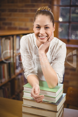 Blonde teacher leaning on pile of books in the library