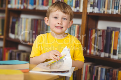 Smiling pupil reading book in the library