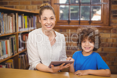 Blonde teacher and pupil using tablet in the library