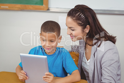 Pretty teacher and pupil using tablet at his desk