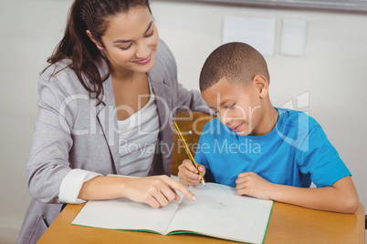 Pretty teacher helping pupil at his desk