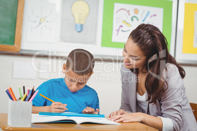 Pretty teacher helping pupil at his desk