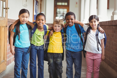 Cute pupils with schoolbags standing at corridor