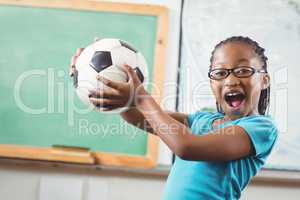 Happy pupil holding football in a classroom