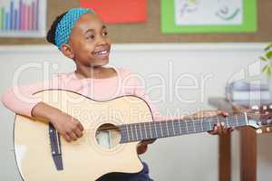 Smiling pupil playing guitar in a classroom