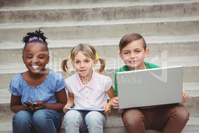 Students sitting on steps and using a tablet and laptop