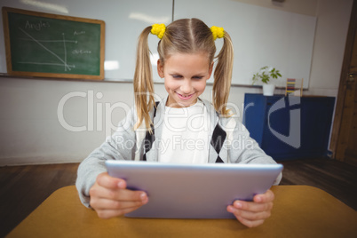Cute pupil using tablet at her desk in a classroom