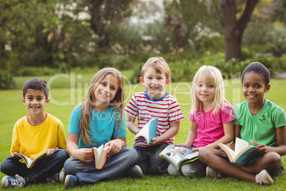 Smiling classmates sitting in grass and holding books