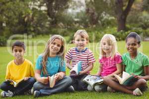 Smiling classmates sitting in grass and holding books