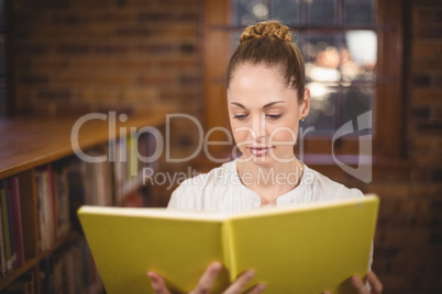 Blonde teacher reading book in the library