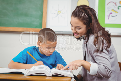 Pretty teacher helping pupil at his desk