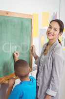 Pretty teacher helping pupil at chalkboard