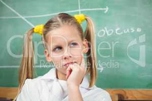 Cute pupil with lab coat thinking in front of chalkboard