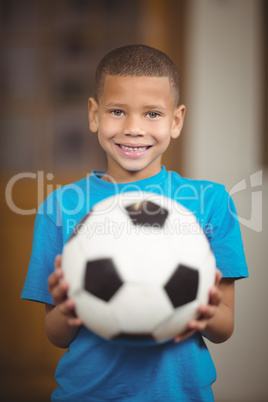 Smiling pupil holding football in a classroom