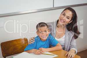 Smiling teacher and her pupil sitting at desk