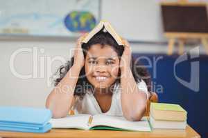 Smiling pupil holding book on head in a classroom