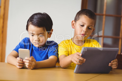 Cute pupils in class using phone and tablet