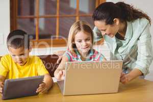 Cute pupils in class using laptop and tablet with teacher