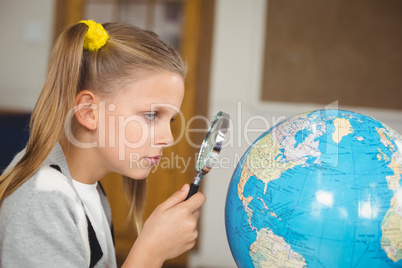 Cute pupil looking at globe through magnifier