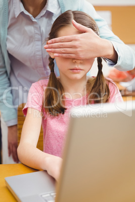 Teacher covering pupils eyes at laptop