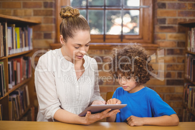 Blonde teacher and pupil using tablet in the library