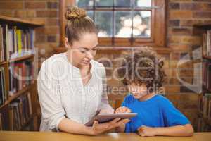 Blonde teacher and pupil using tablet in the library
