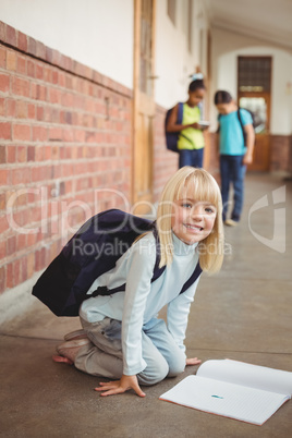 Cute pupil kneeling over notepad at corridor